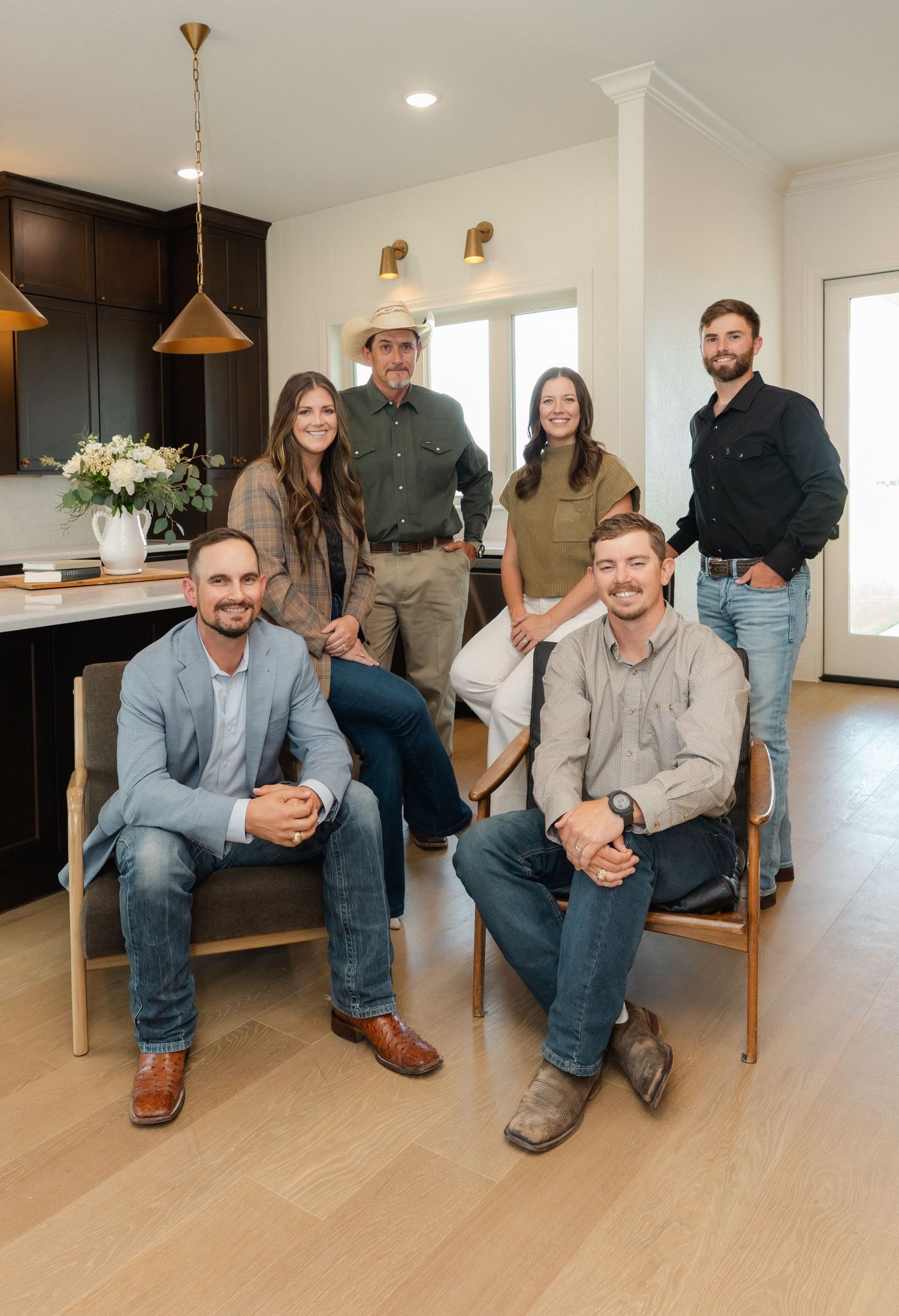 A professional real estate team of six people posing together in a modern home with dark cabinets and hardwood floors.
