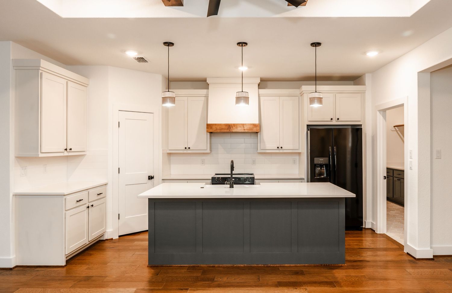 Spacious kitchen with white cabinets, gray island, pendant lights, and dark hardwood floors.