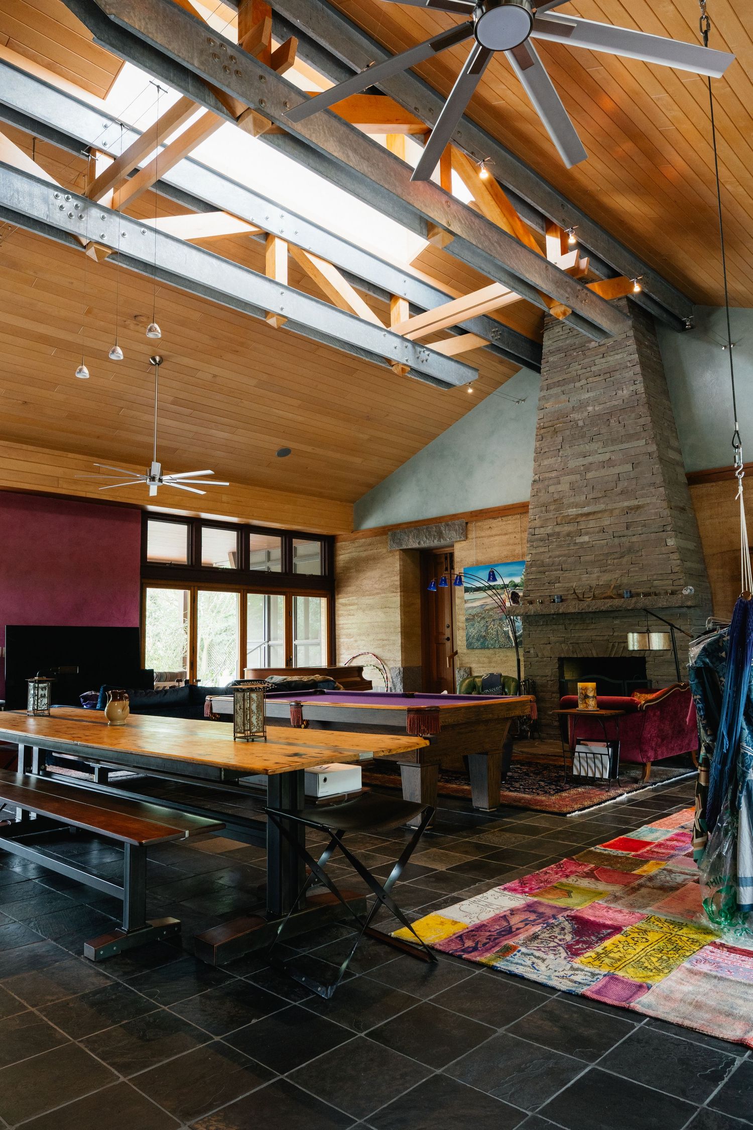 Spacious open-plan living area with vaulted wood ceiling, exposed beams, pool table, fireplace, and industrial dining table.