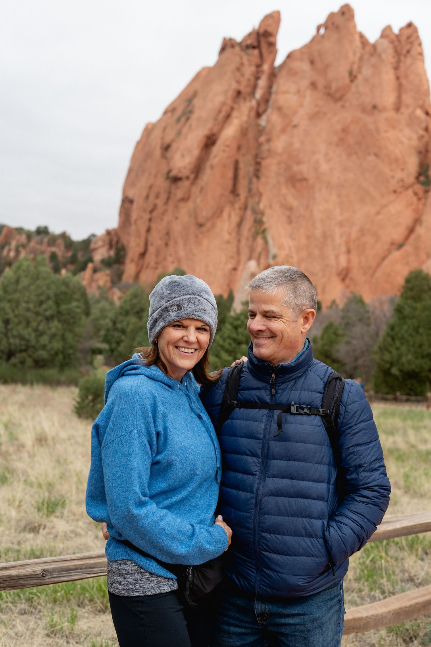 Smiling couple in winter jackets poses before towering red rock formations at Garden of the Gods park.