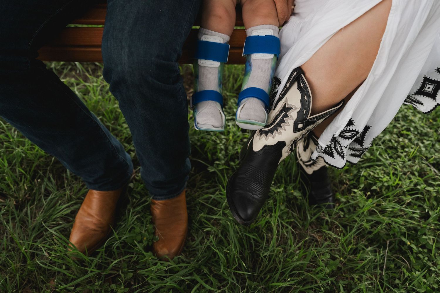 Close-up of cowboy boots and striped toddler socks worn by a family sitting on a swing.