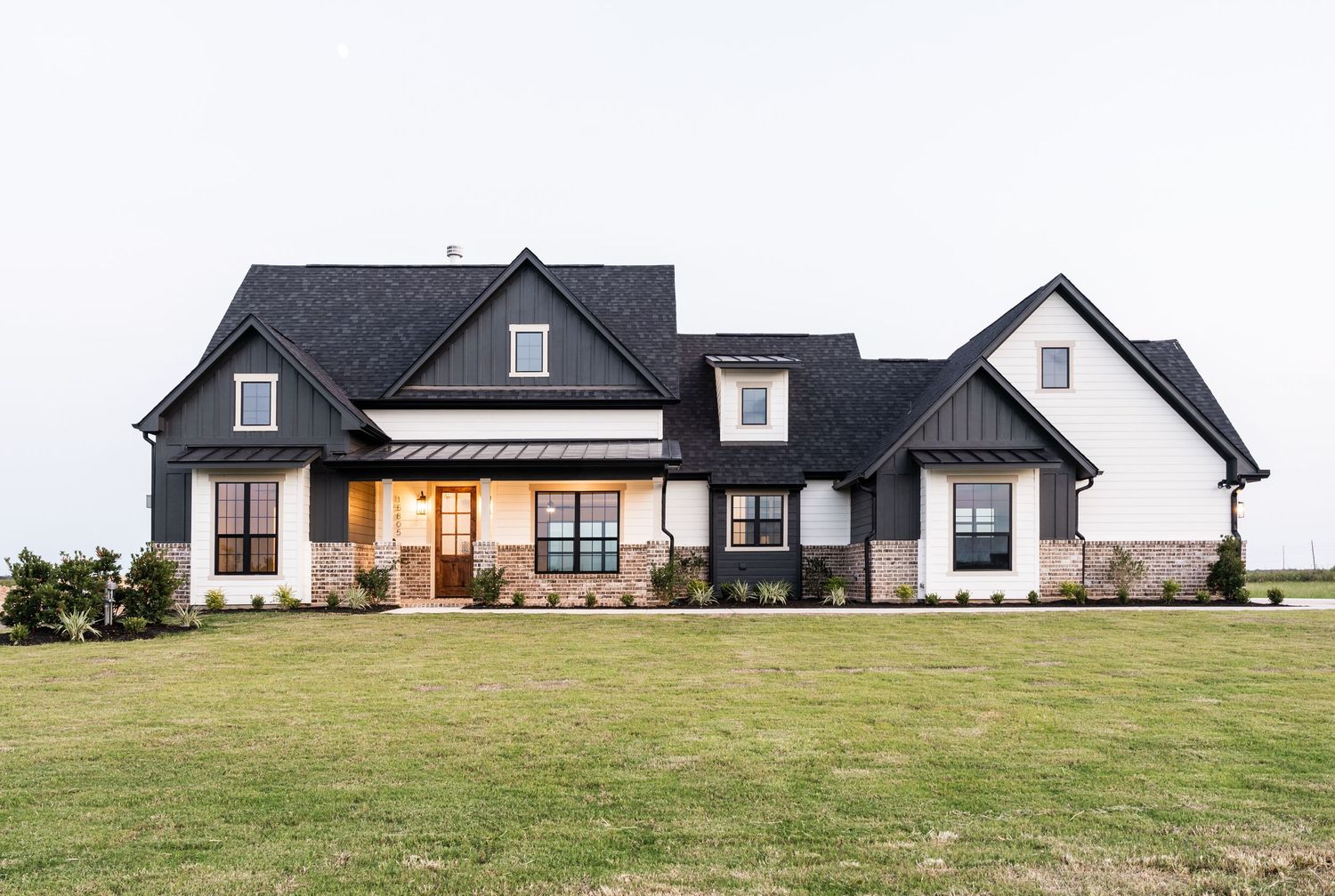 Modern farmhouse with black roof, white siding, stone accents, and large front lawn.