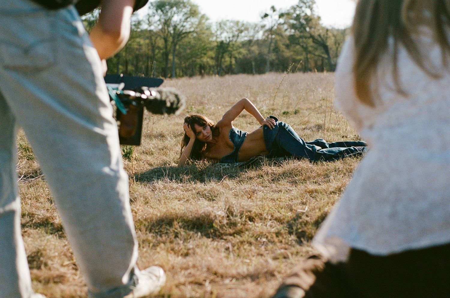 Model posing in a dry grass field during an outdoor photo shoot with crew members.