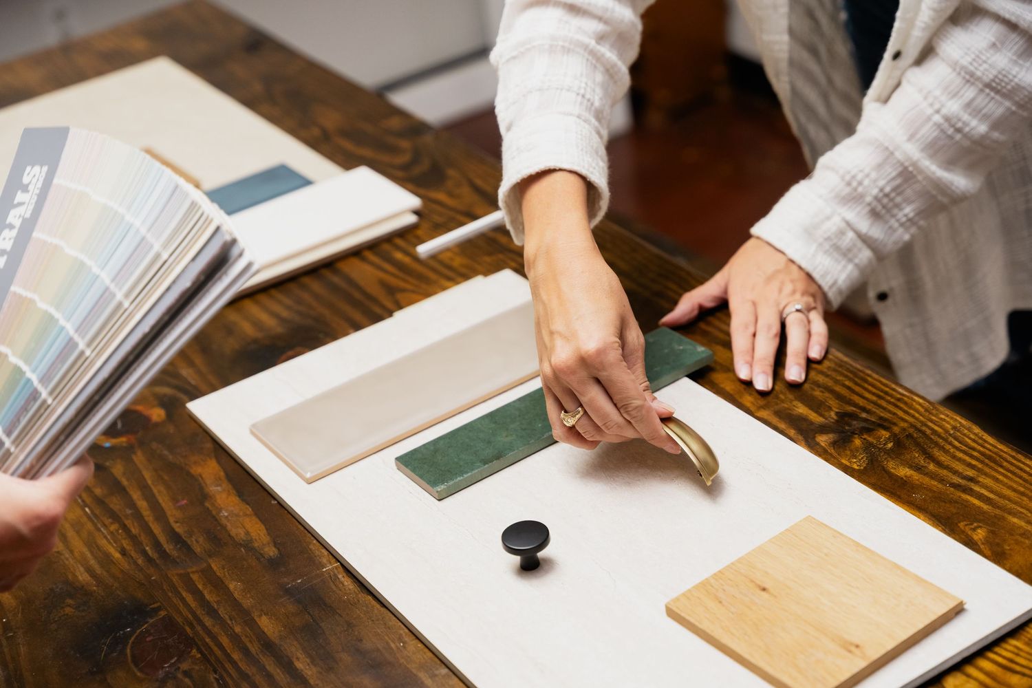 Interior designer presenting material samples, hardware, and color swatches on a wooden table.