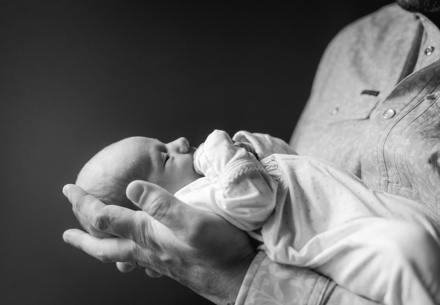 Black and white photo of a newborn baby resting peacefully in an adult's supportive hands.