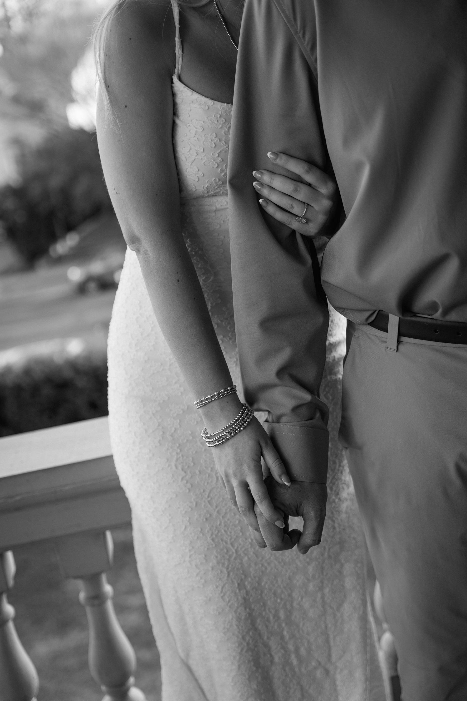 Black and white photo of a bride and groom holding hands, showcasing her diamond ring and bracelets in a romantic pose.