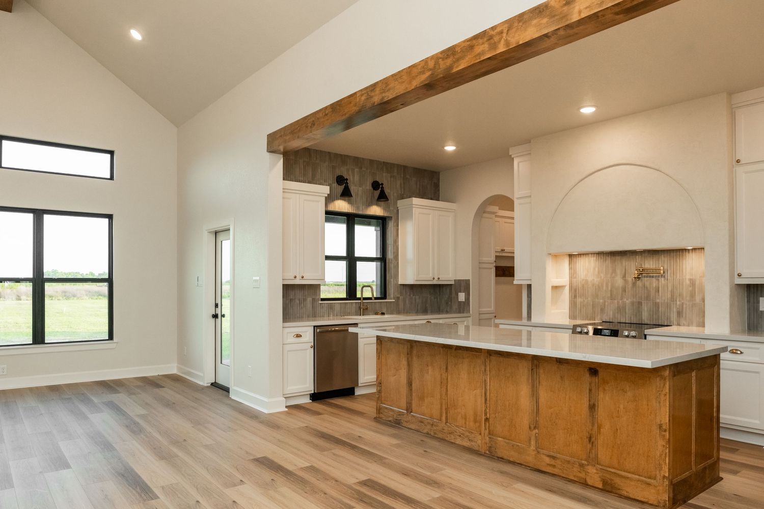 Modern farmhouse kitchen with wood beam ceiling, white cabinets, rustic island, and light hardwood floors.