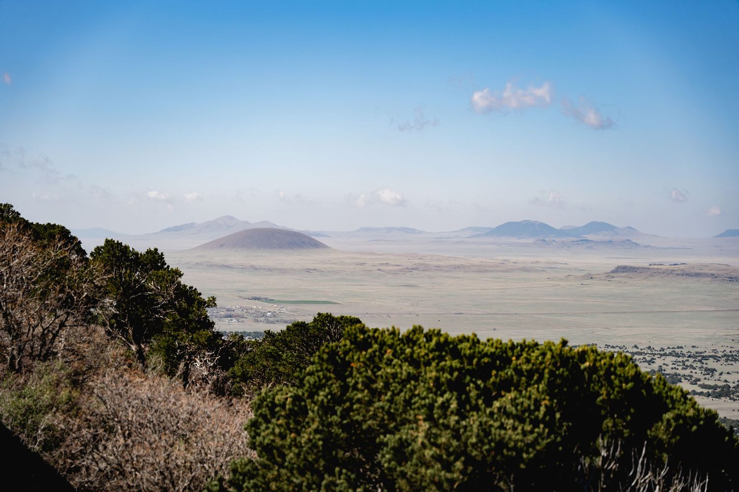 Panoramic landscape view of vast African savanna with distant volcanic mountains under a hazy blue sky.