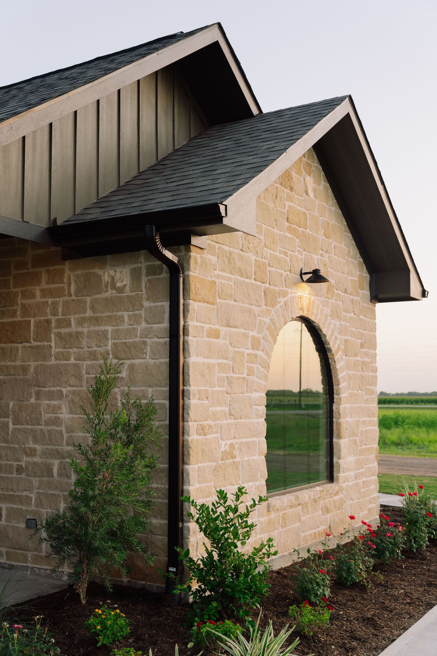 Texas limestone exterior home facade with arched window, black trim, and lush landscaping at twilight.