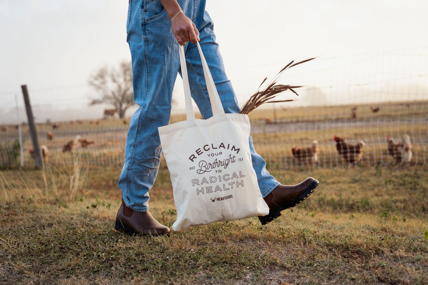 Person carrying a canvas tote bag reading Reclaim Your Birthright Radical Health on a farm.