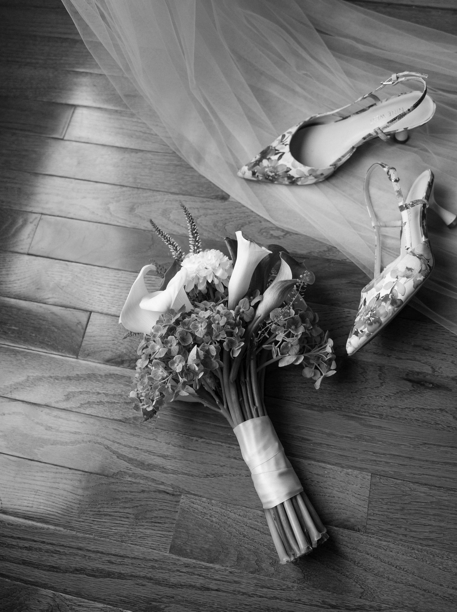 Black and white photo of bridal bouquet and floral heels on wood floor.