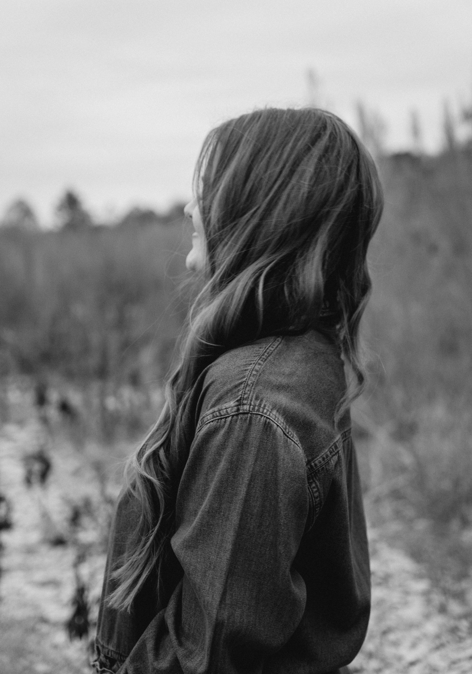 Black and white profile portrait of a woman with long wavy hair wearing a denim jacket outdoors.