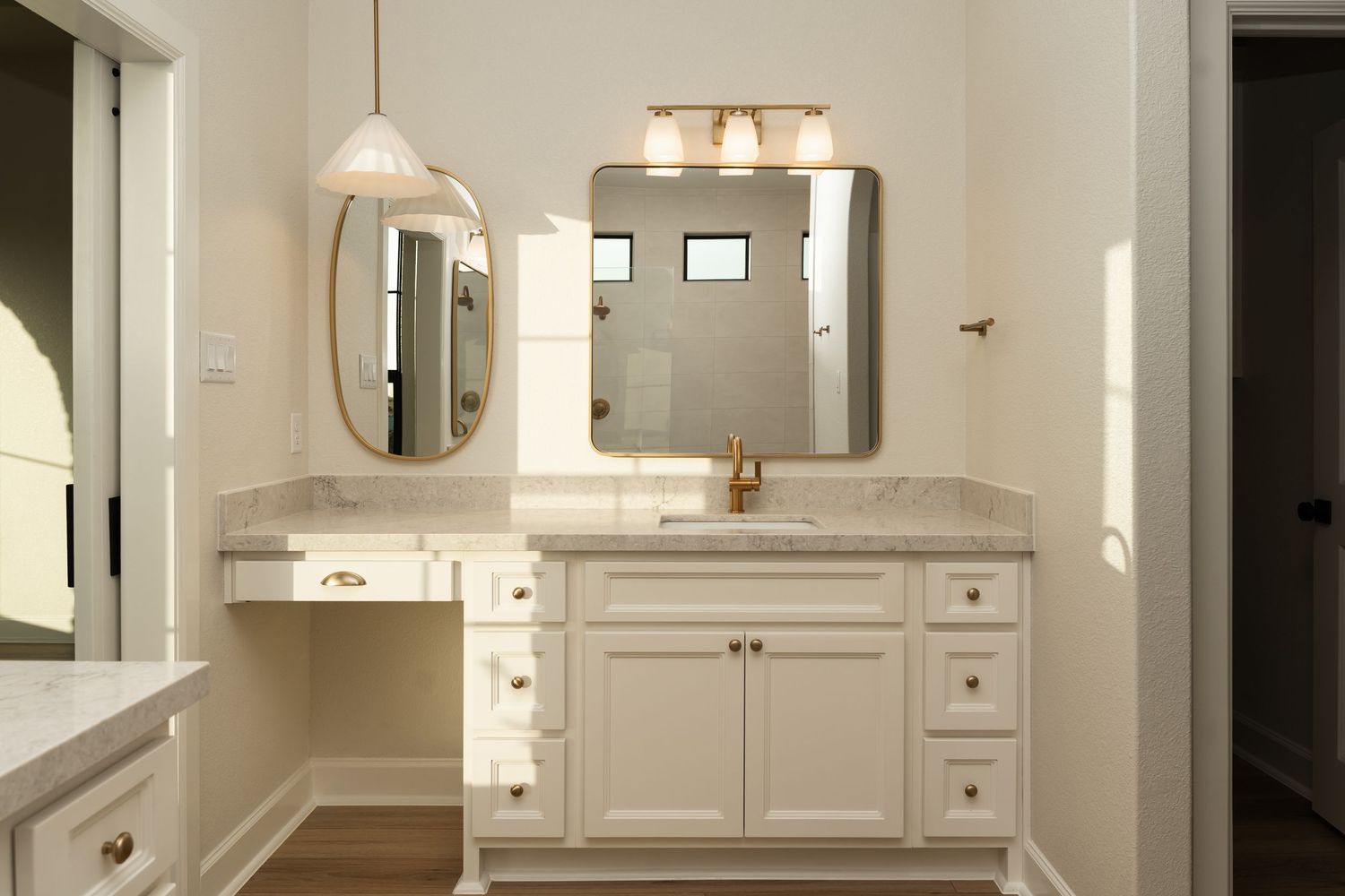 White bathroom vanity with marble countertop, gold hardware, oval pendant light, and rectangular wall mirror.