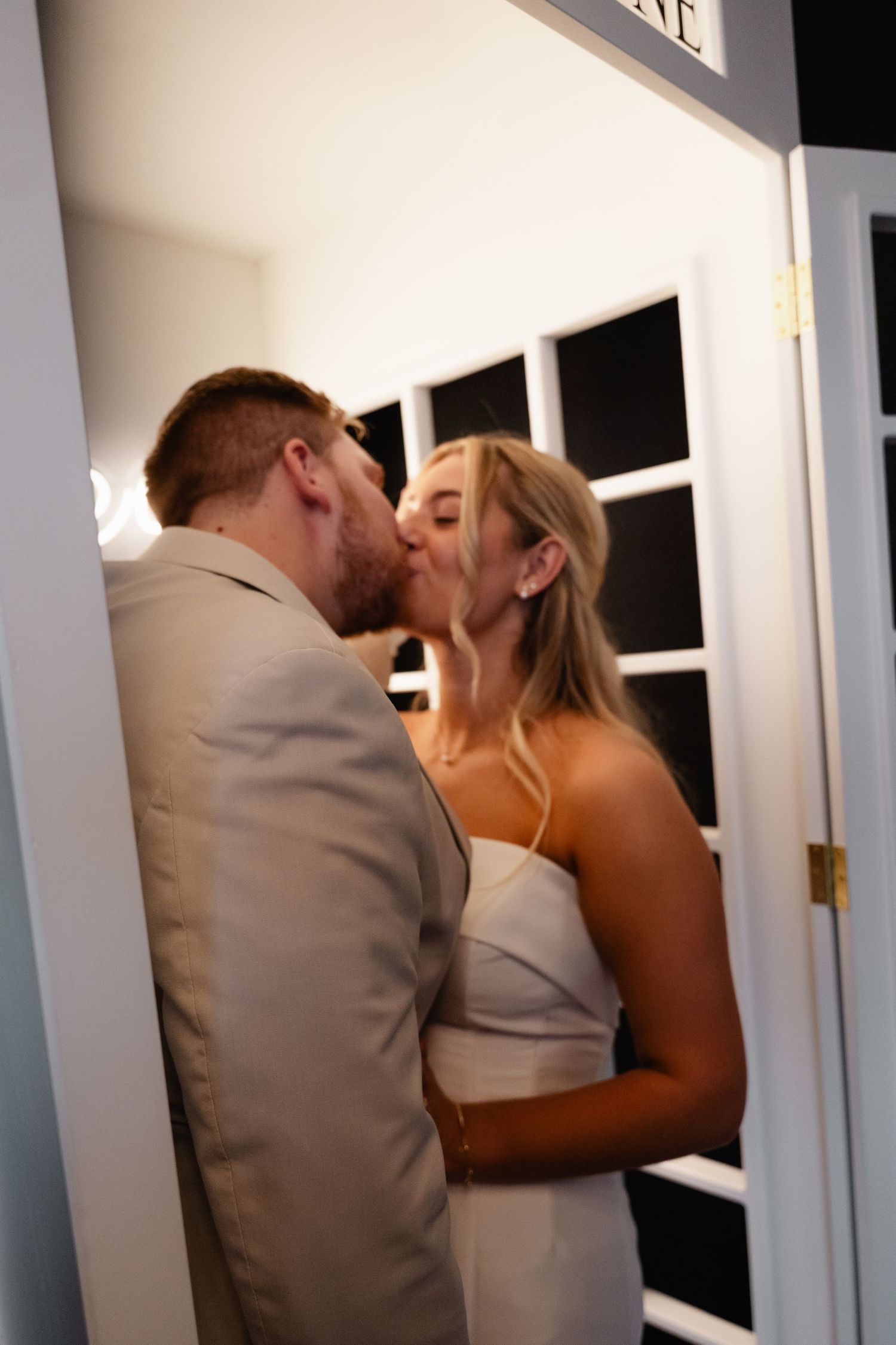 Bride and groom share a romantic kiss in a doorway during their wedding celebration.