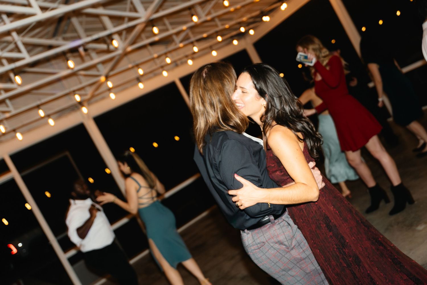 Wedding guests share a romantic kiss while dancing together at an evening outdoor reception.