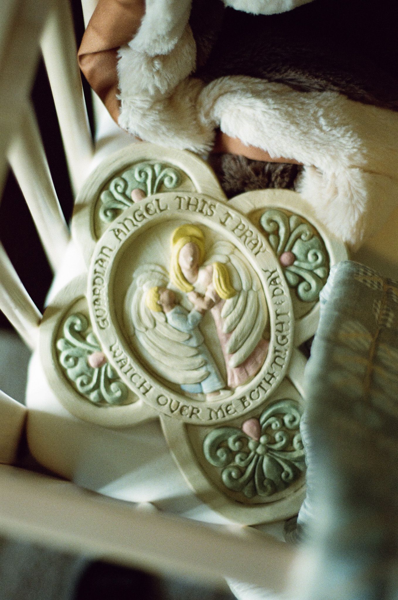 Ceramic Guardian Angel prayer plaque resting in a white crib with a soft stuffed animal.