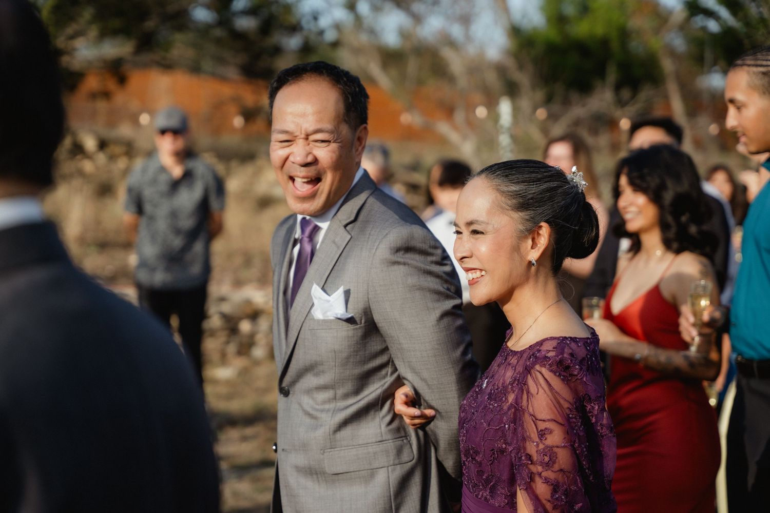 Joyful father of bride laughing with elegantly dressed woman at outdoor wedding.