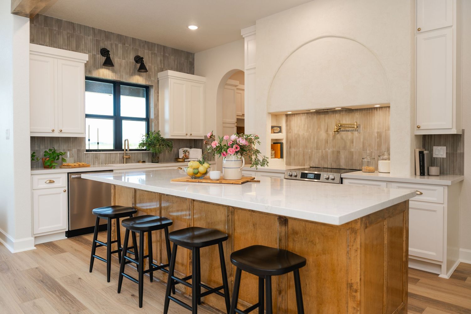Farmhouse kitchen with white cabinets, wood island, black bar stools, arched doorway, and quartz countertops.