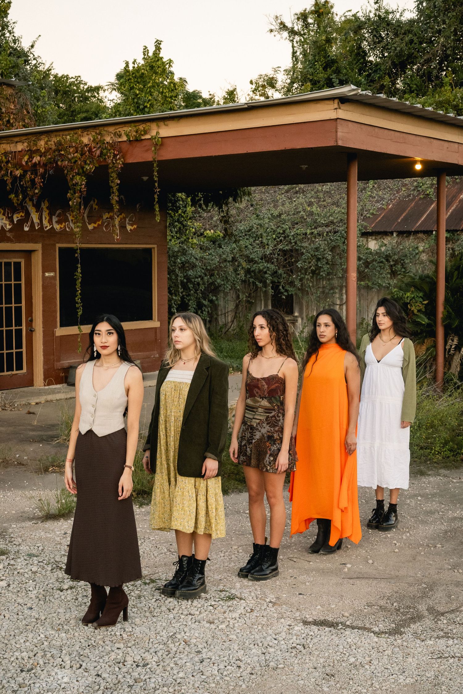 Five women in boho fashion standing outside a rustic cafe at dusk.