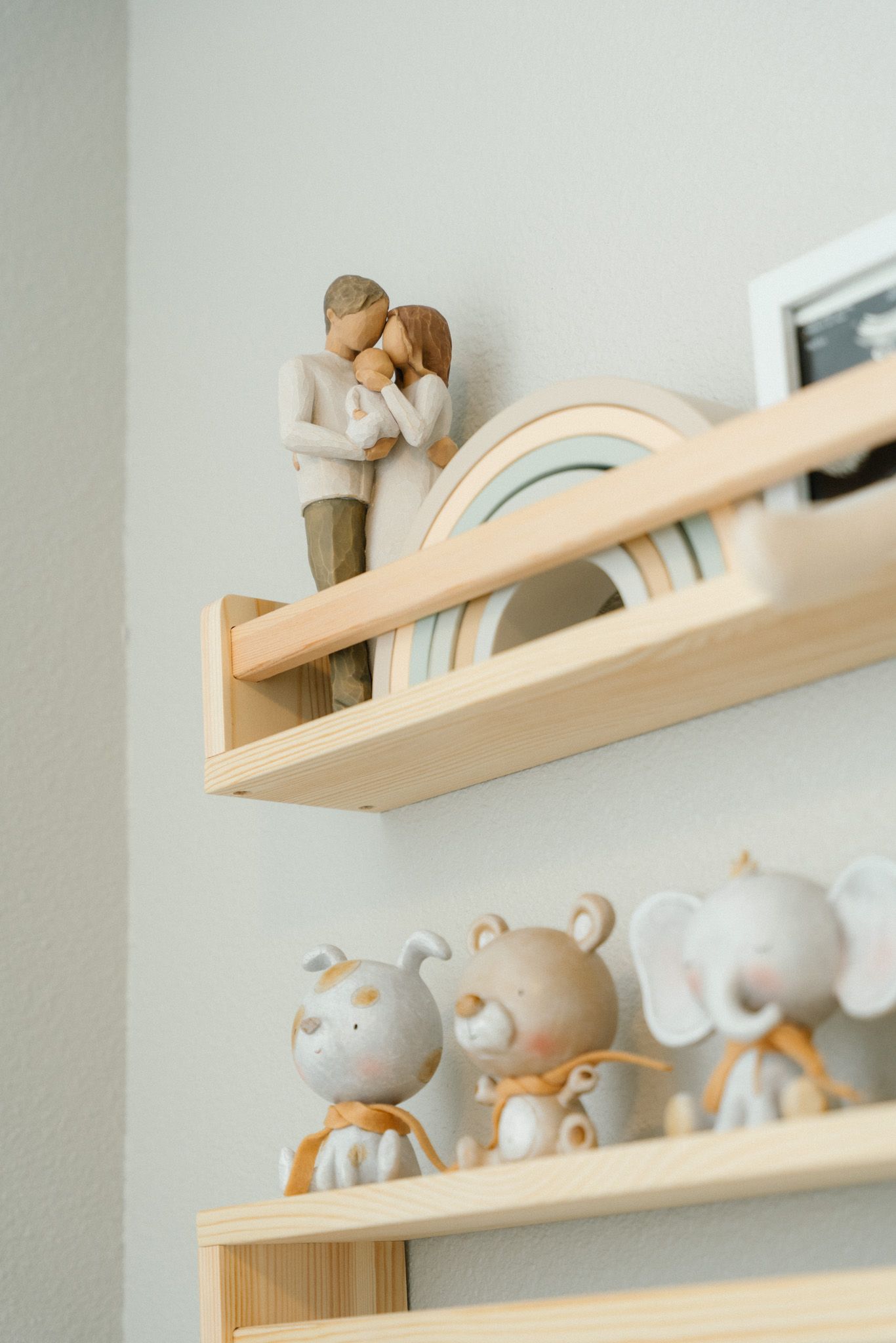 Wooden nursery shelves displaying a couple figurine, rainbow decor, and cute animal figurines.