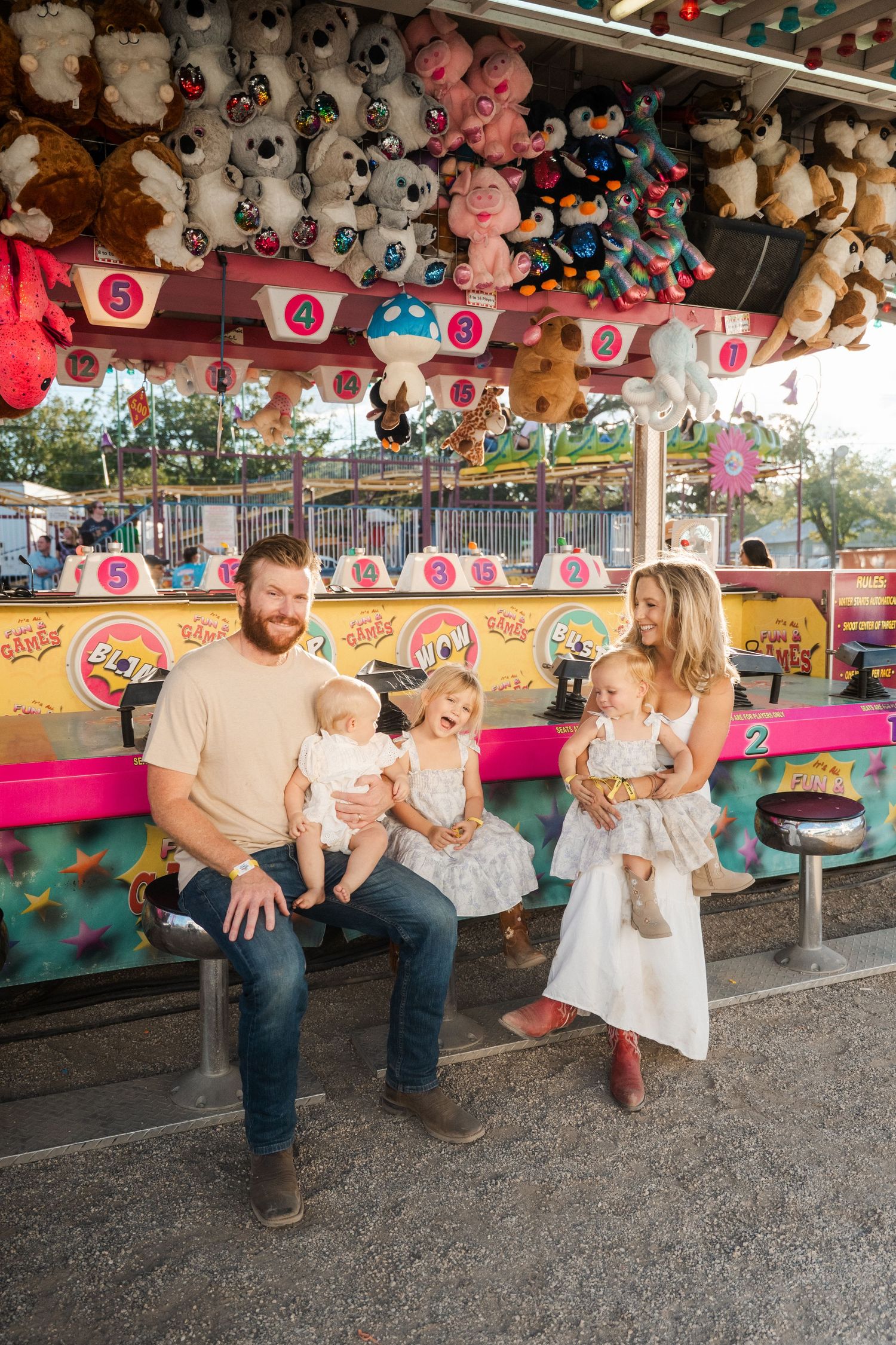 Family of five posing at carnival game booth with stuffed animal prizes in background.