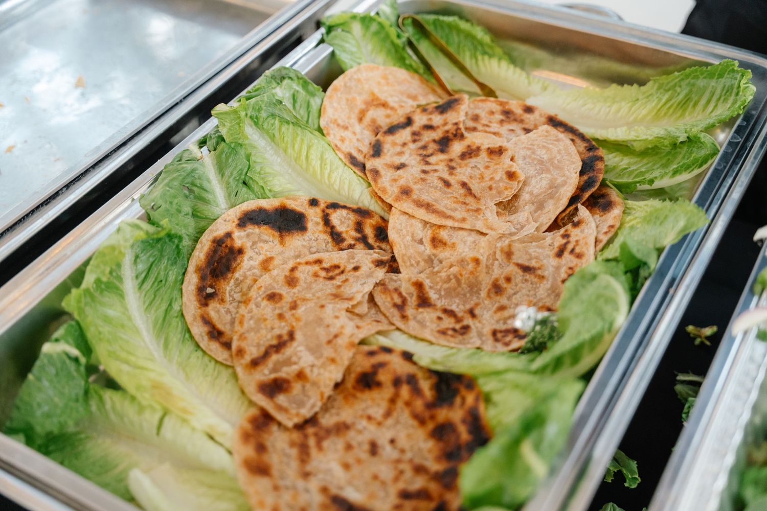 Grilled flatbreads served on fresh romaine lettuce leaves in a catering tray.