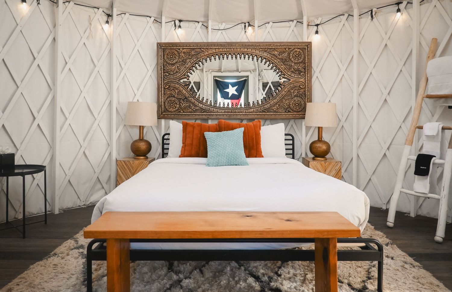 Cozy yurt bedroom with a king bed, Texas flag headboard art, orange pillows, and string lights.