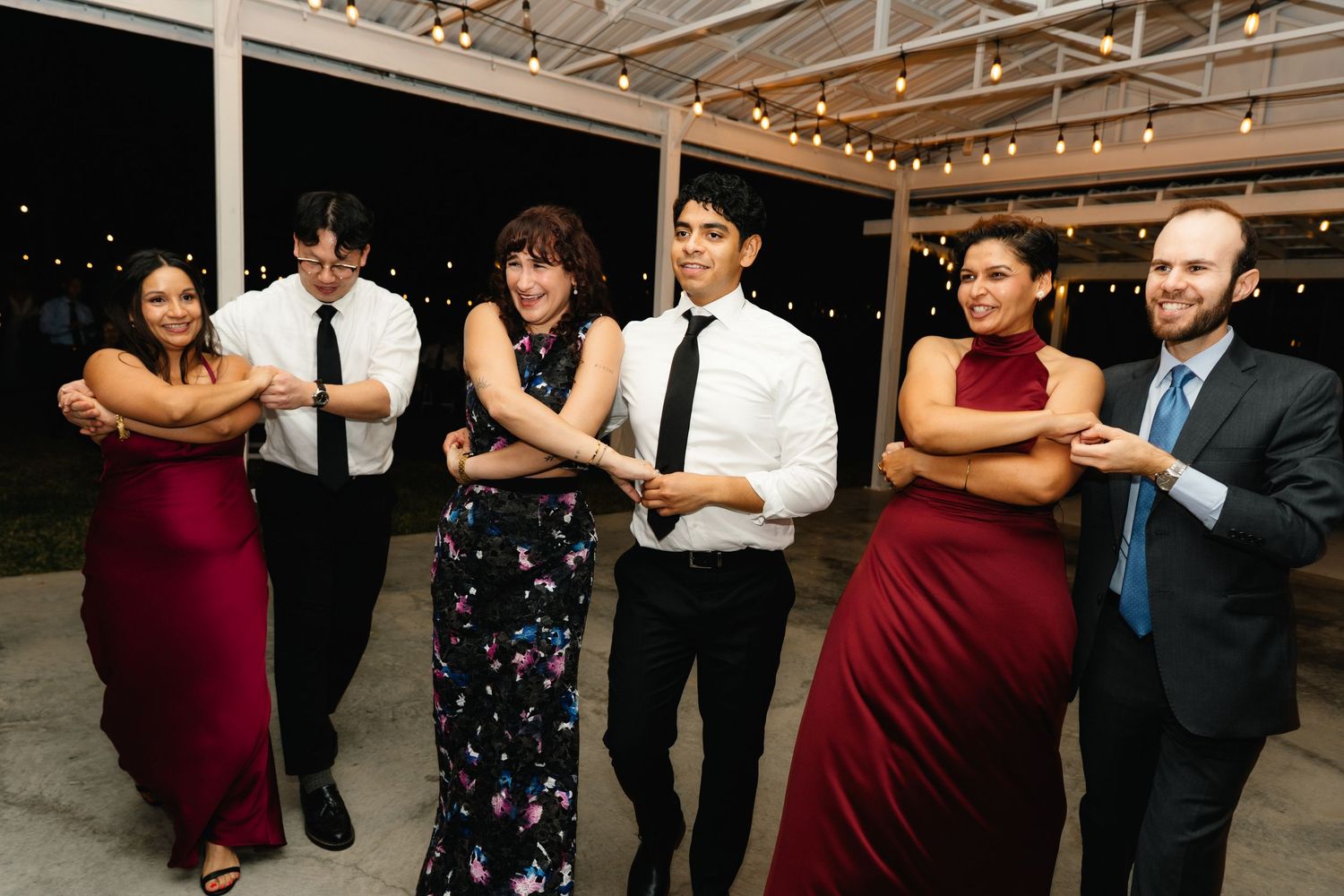 Six wedding guests pose playfully in a line on the dance floor at an evening reception.