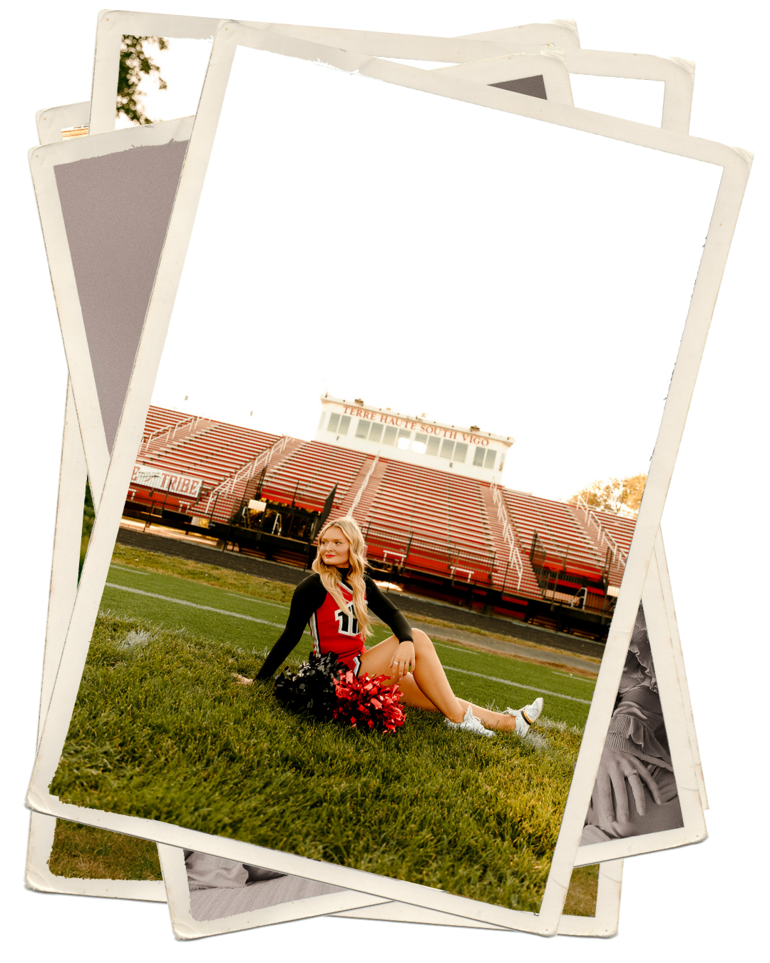 A cheerleader in uniform sits on a football field grass holding red pom-poms with a stadium in the background.