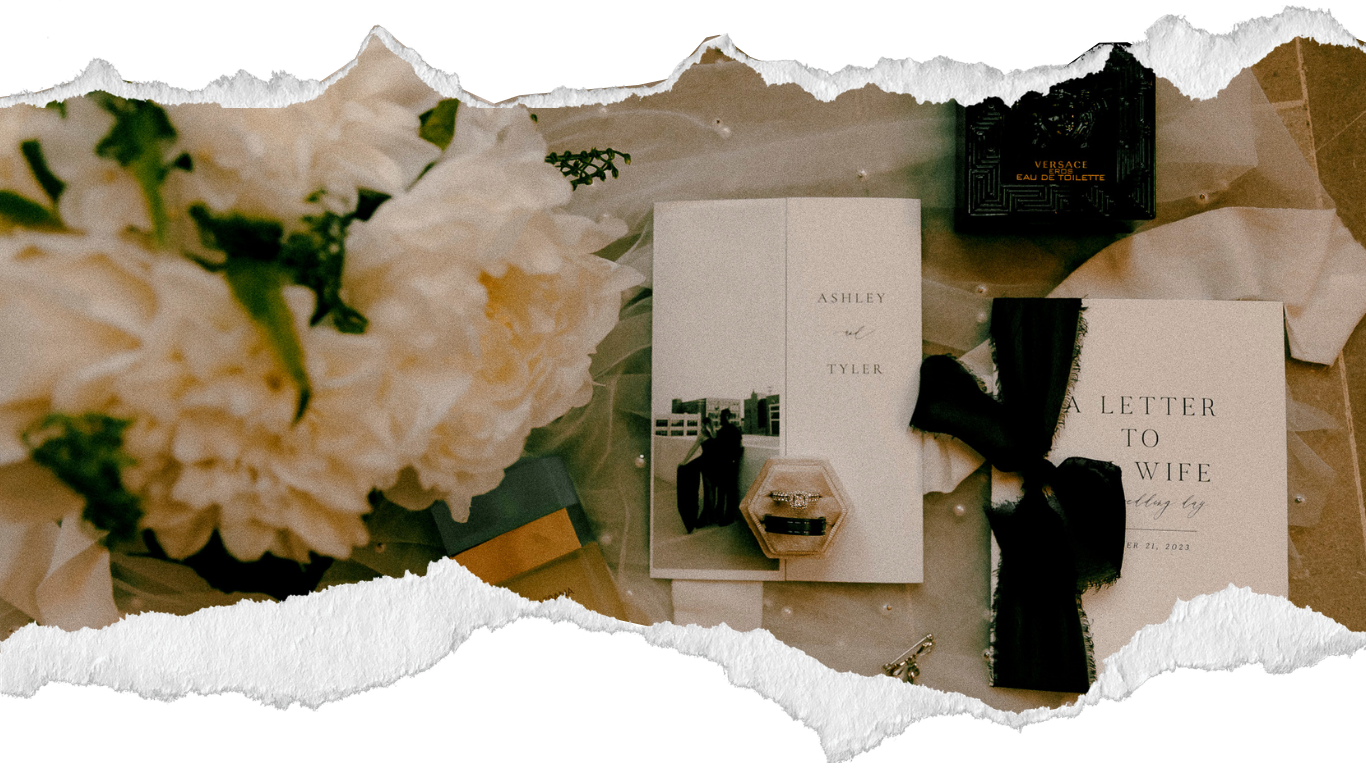 Elegant flat lay with white peonies, a wedding book, and black ribbon on a neutral background.