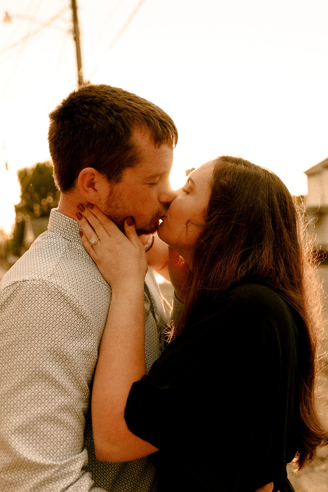 A couple shares a romantic kiss at golden hour, with the woman tenderly holding the man's face in her hands.