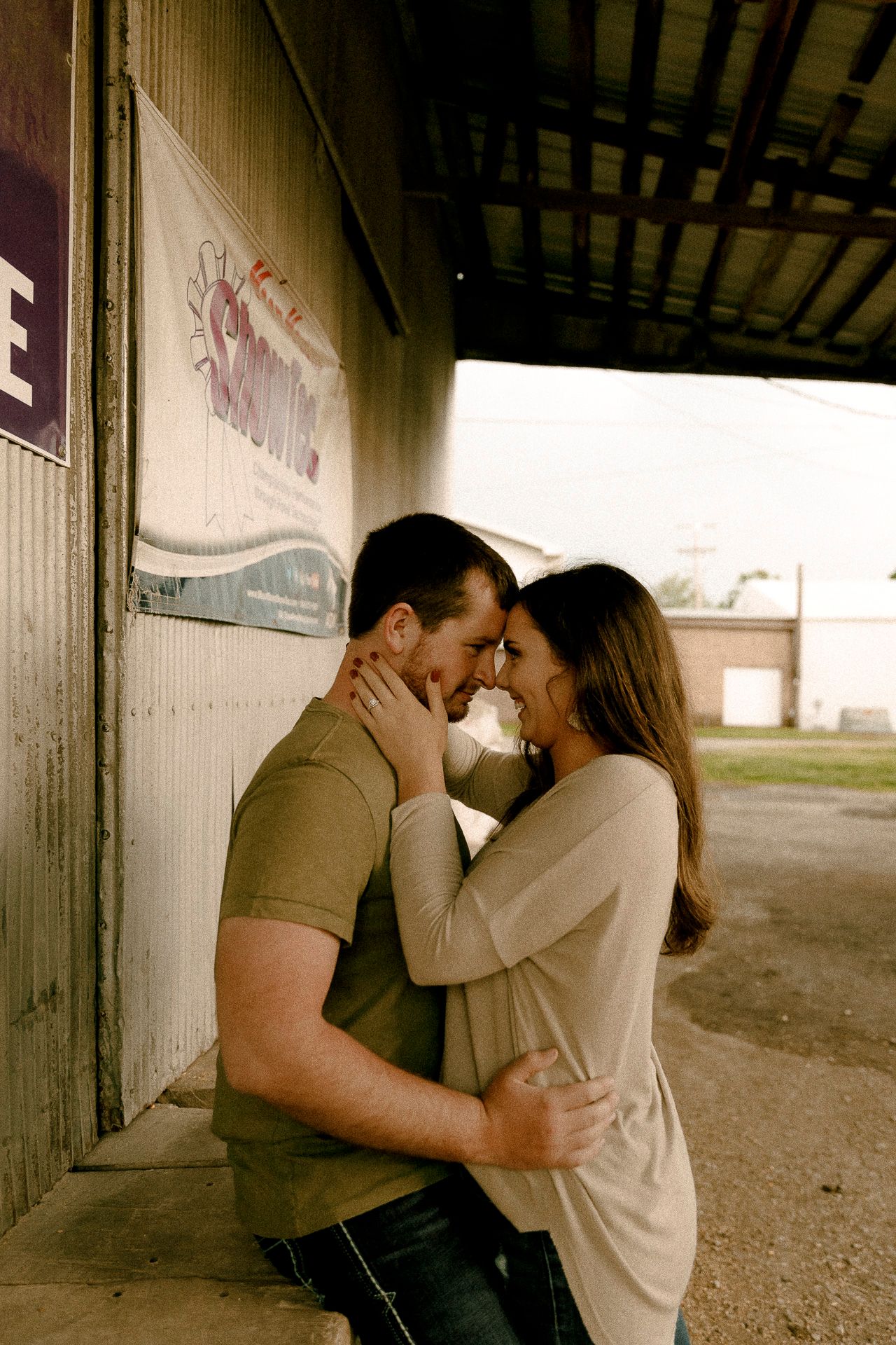 Couple sharing a romantic embrace and almost kissing against a rustic building wall outdoors.