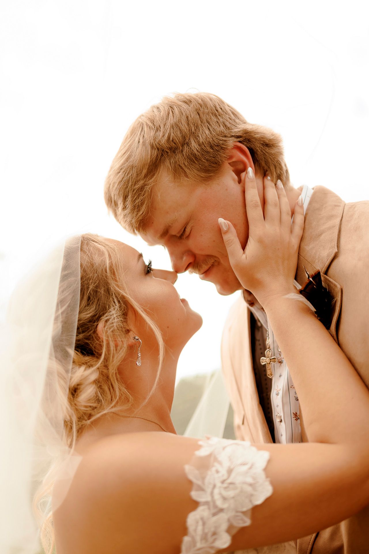 A bride and groom share a romantic almost-kiss moment on their wedding day, with the bride wearing a lace veil.