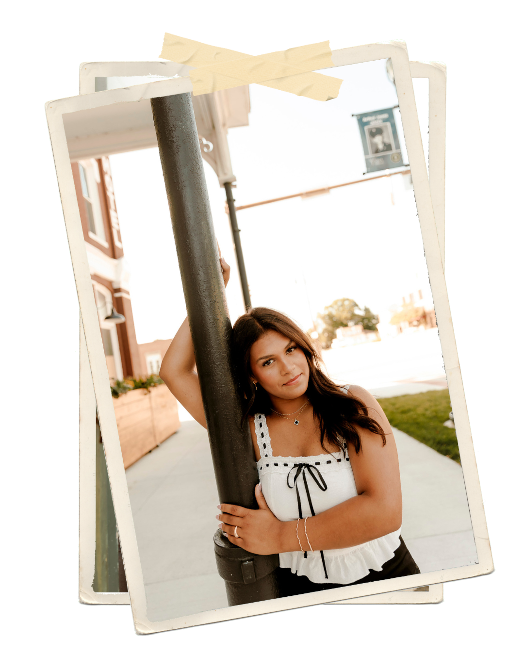 Young woman in white top leaning against a metal pole on a sunny urban street, senior portrait photography.