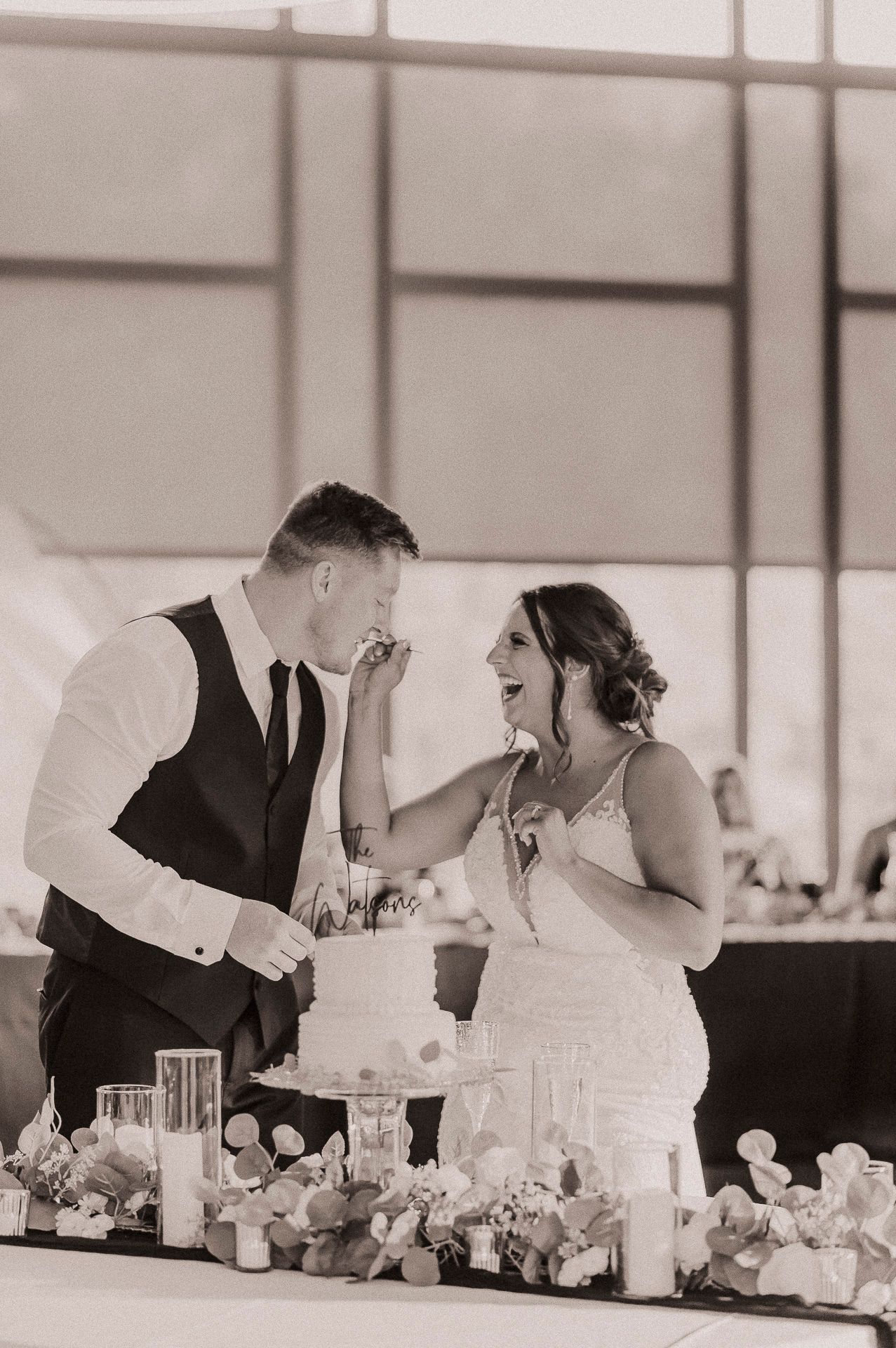 Bride and groom cutting wedding cake together in black and white photo at elegant reception venue.
