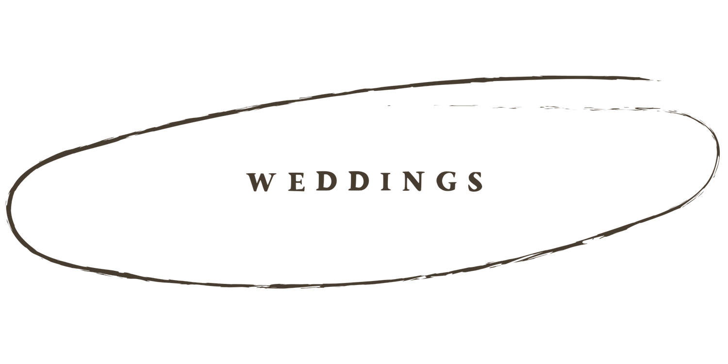 A couple in formal wedding attire stands in a rustic barn doorway with natural light streaming in from behind.