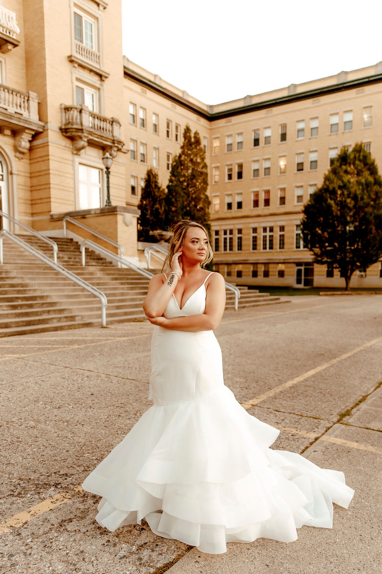 A bride in a flowing white dress twirls and dances joyfully outside a grand stone building on her wedding day.