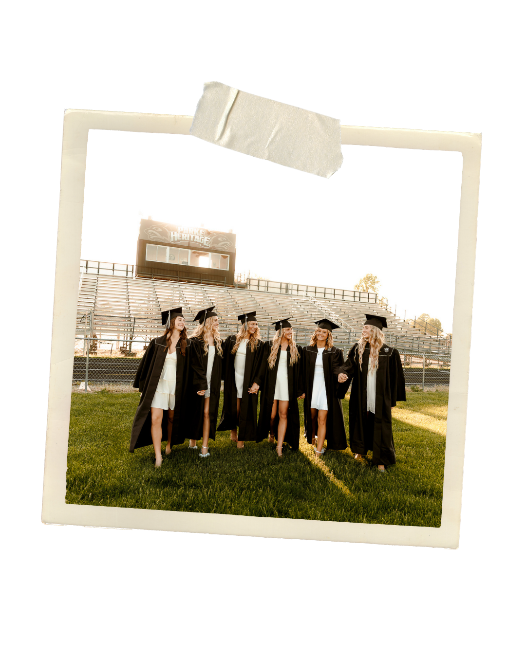 Group of high school graduates in black caps and gowns posing on a football field stadium.