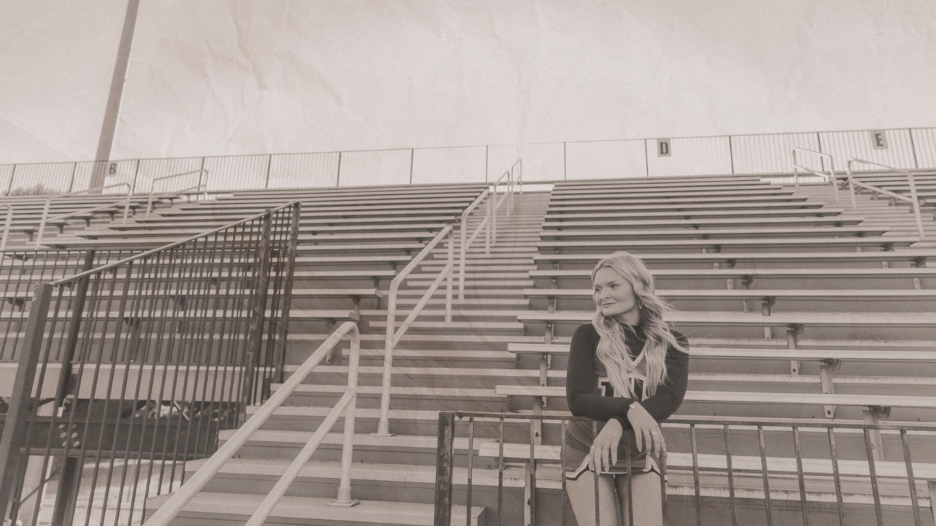 Young woman posing on bleacher stairs at an outdoor sports stadium in a black and white photo.