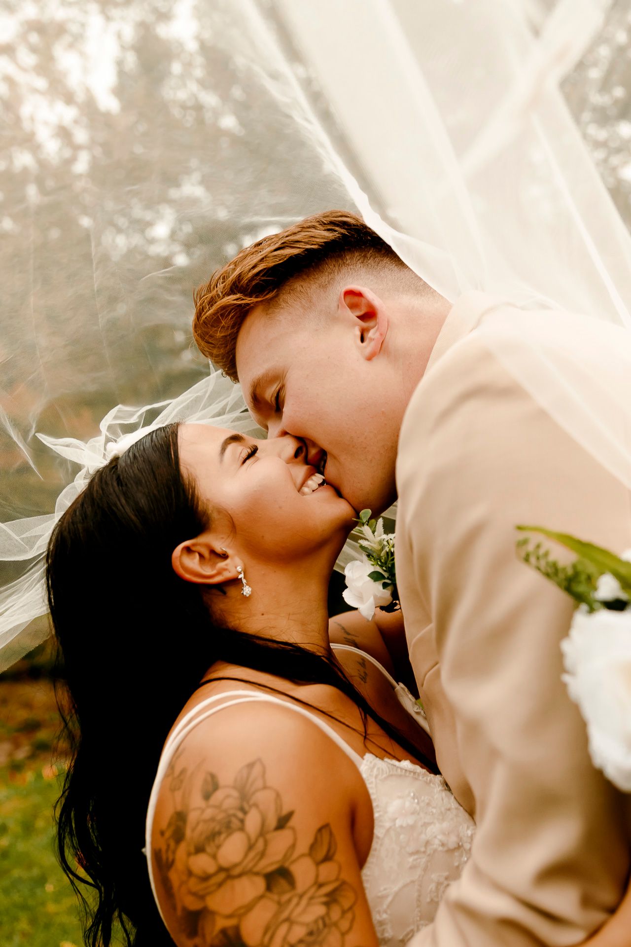 A bride and groom share a romantic kiss under a flowing white veil on their wedding day.