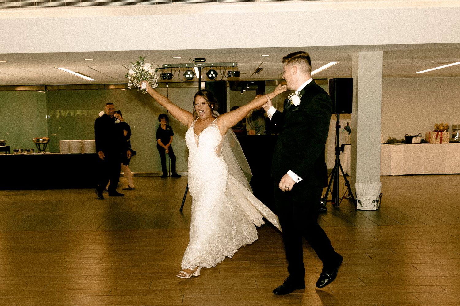 Bride and groom share their first dance, bride holding bouquet aloft in elegant wedding venue.