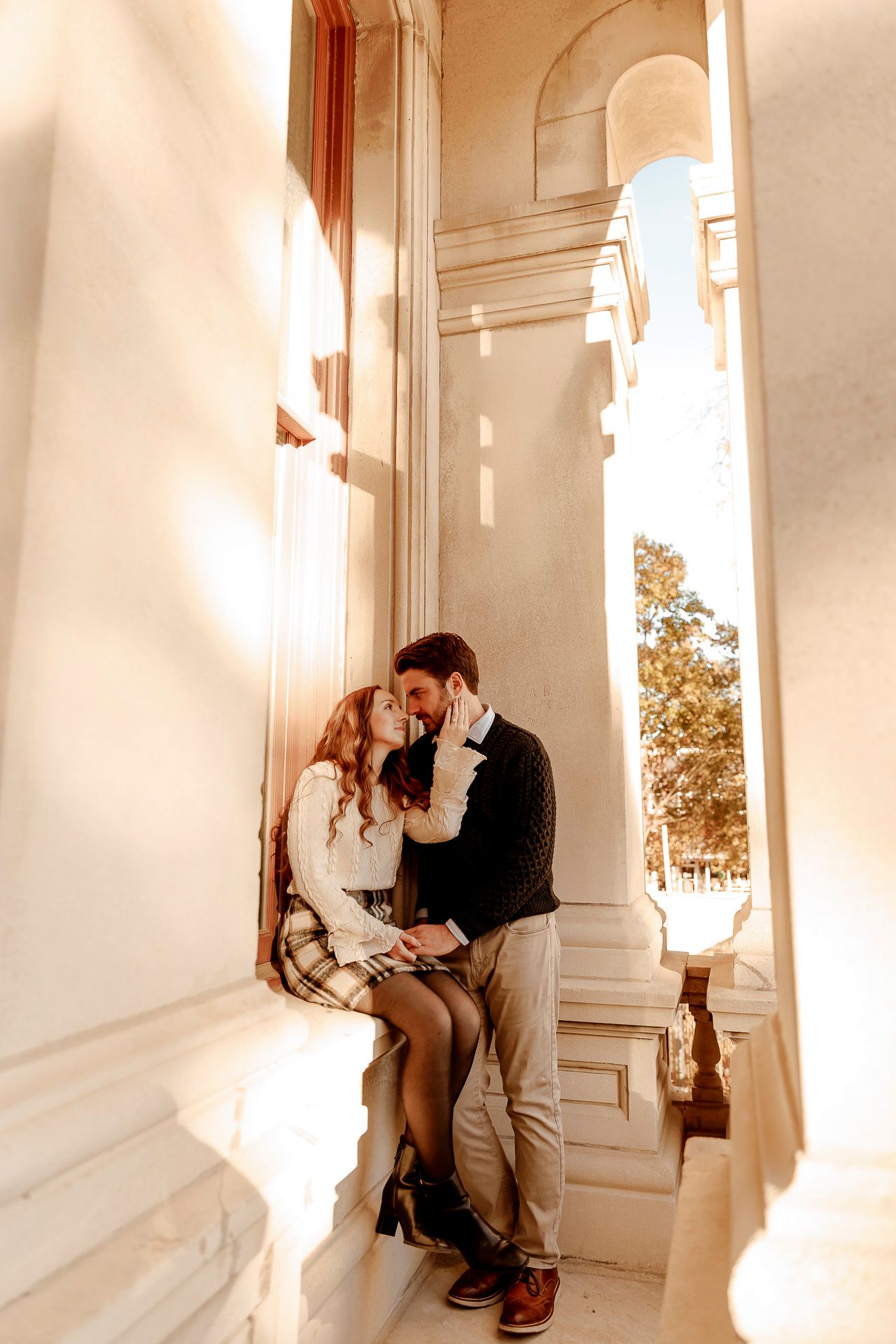Romantic couple embraces in a sunlit white hallway with columns creating a dreamy atmosphere.