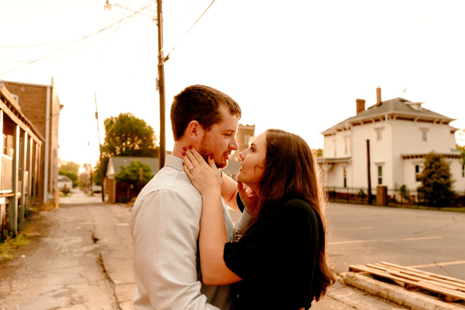 Couple sharing a romantic almost-kiss embrace on a charming small town street at golden hour sunset.