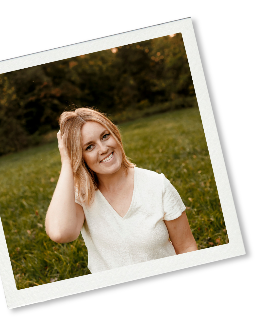 Smiling young woman with blonde hair in white top sitting outdoors on green grass in warm natural light.