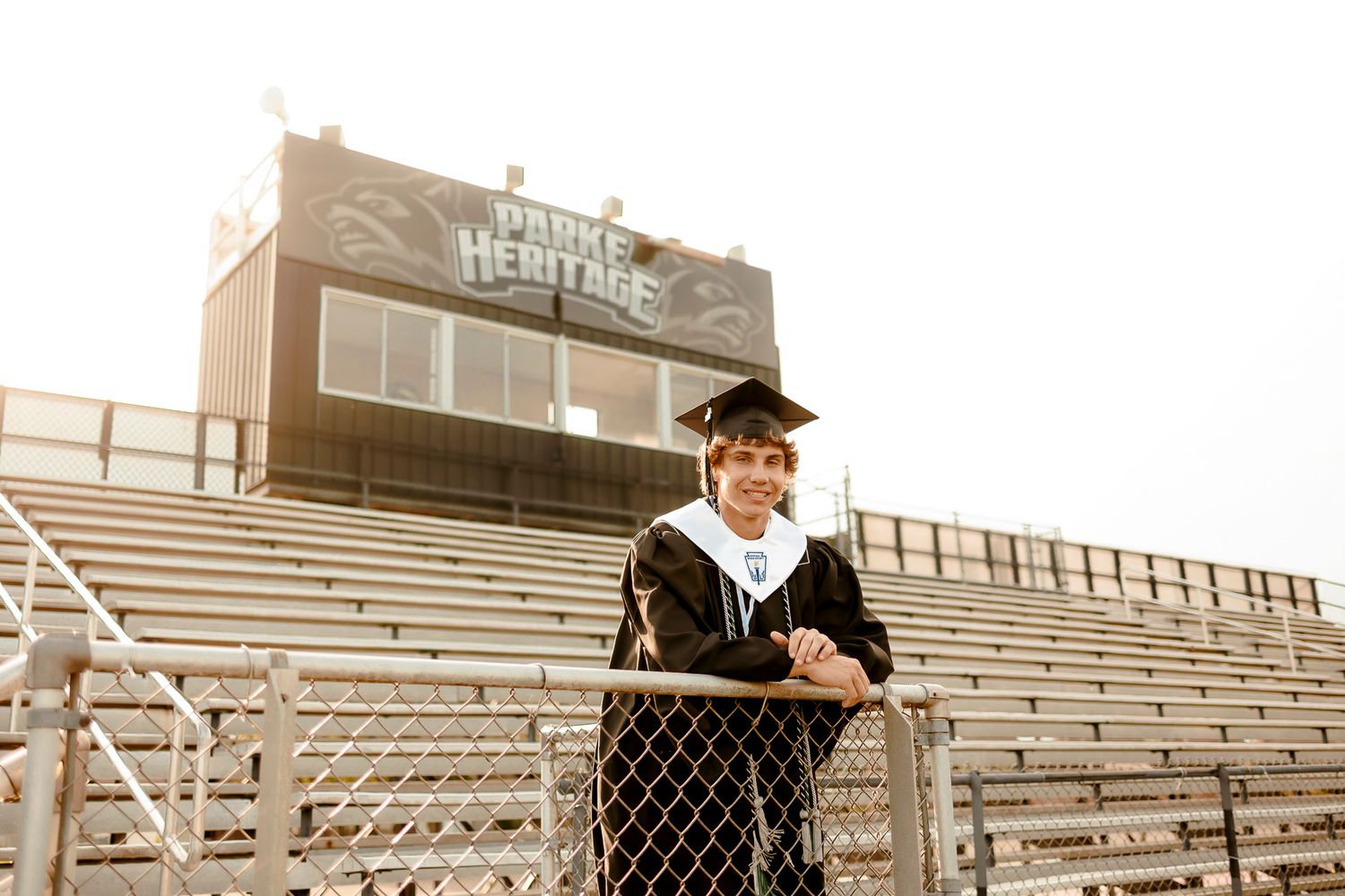 Graduate in cap and gown smiling at Parker Heritage High School stadium during senior portrait session.