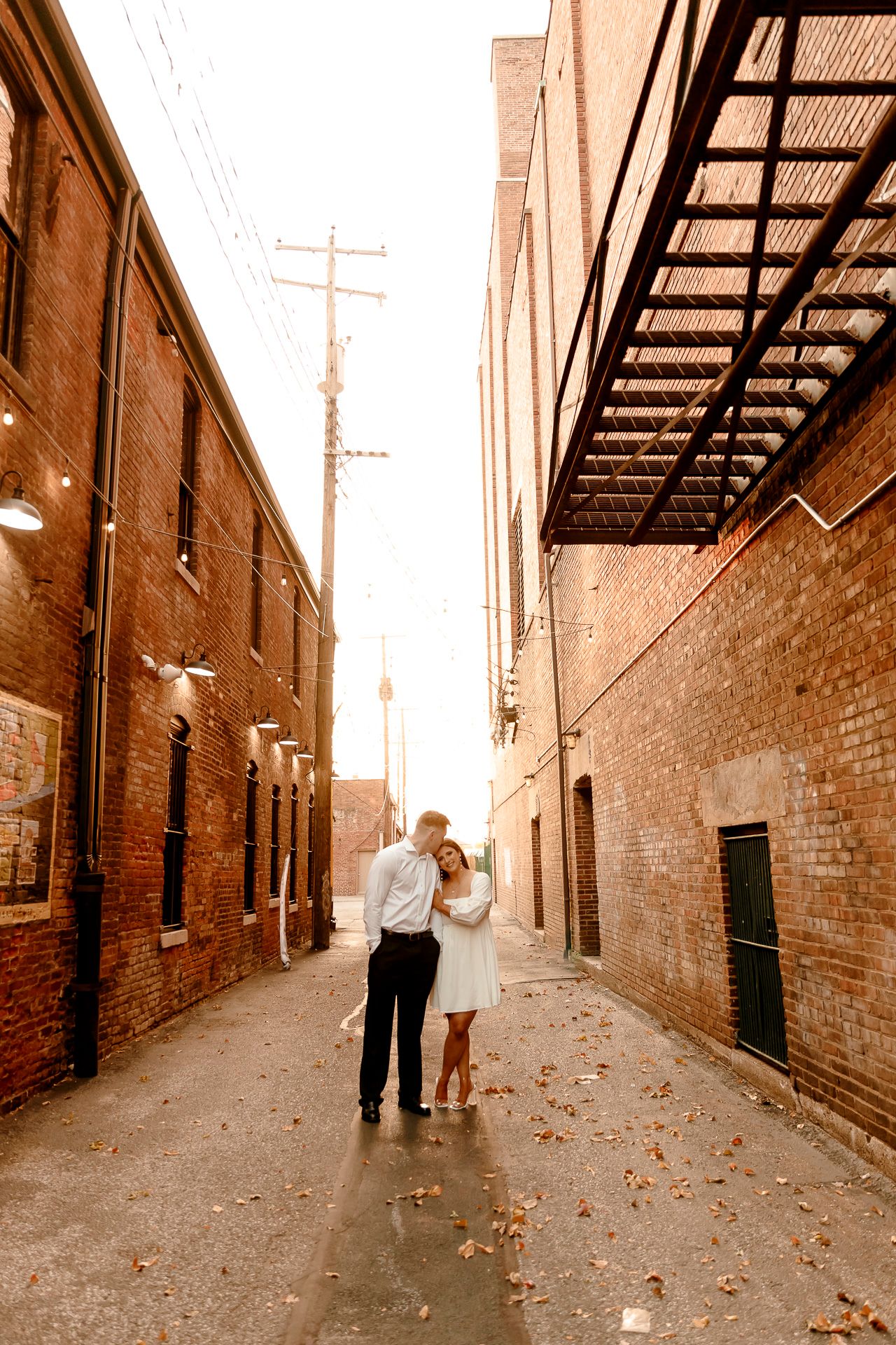Couple embracing romantically in a charming brick alley, wet pavement reflecting warm lights in an urban setting.