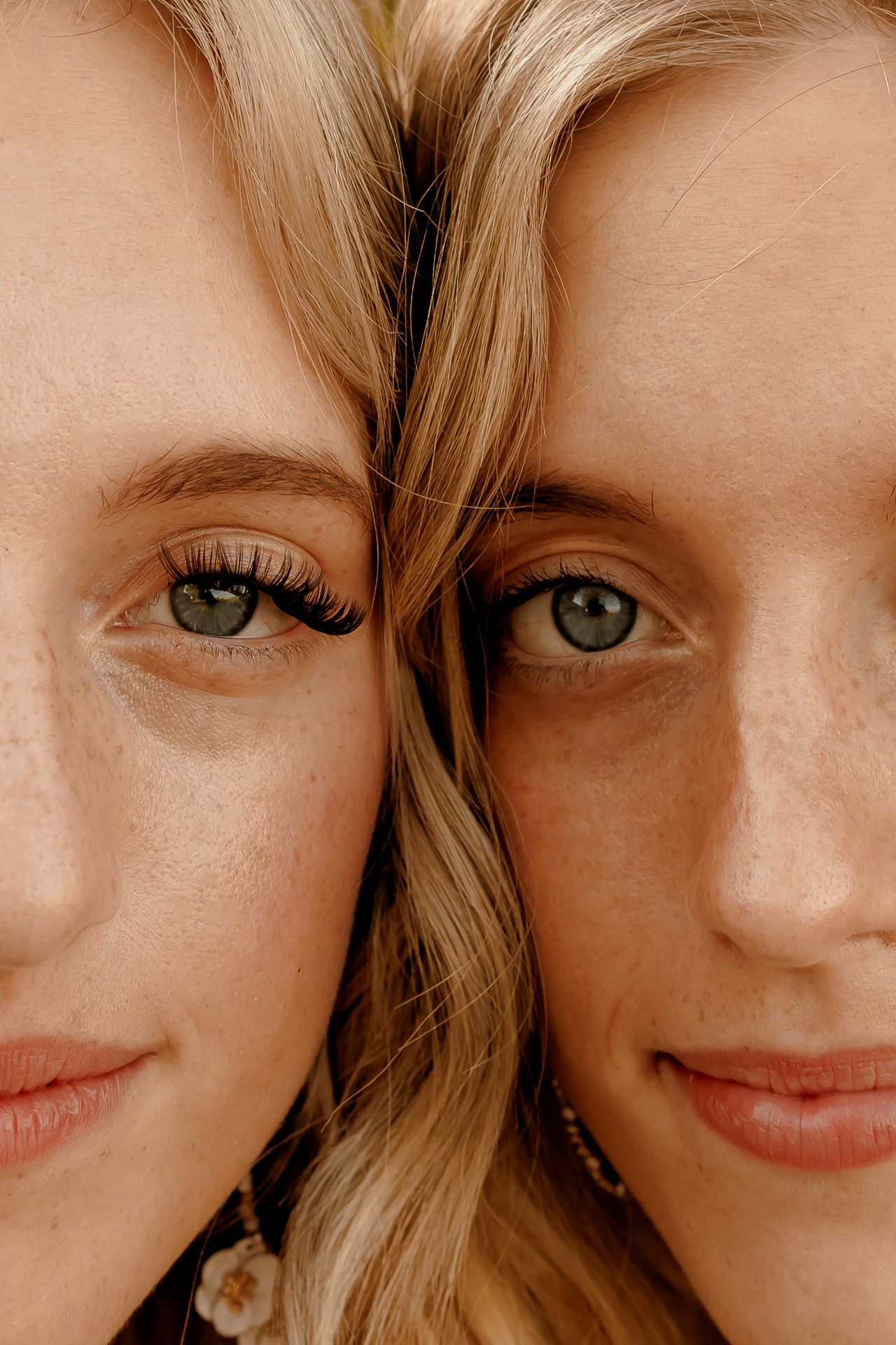 Close-up portrait of two blonde women with green eyes and freckles posing cheek to cheek, smiling softly.