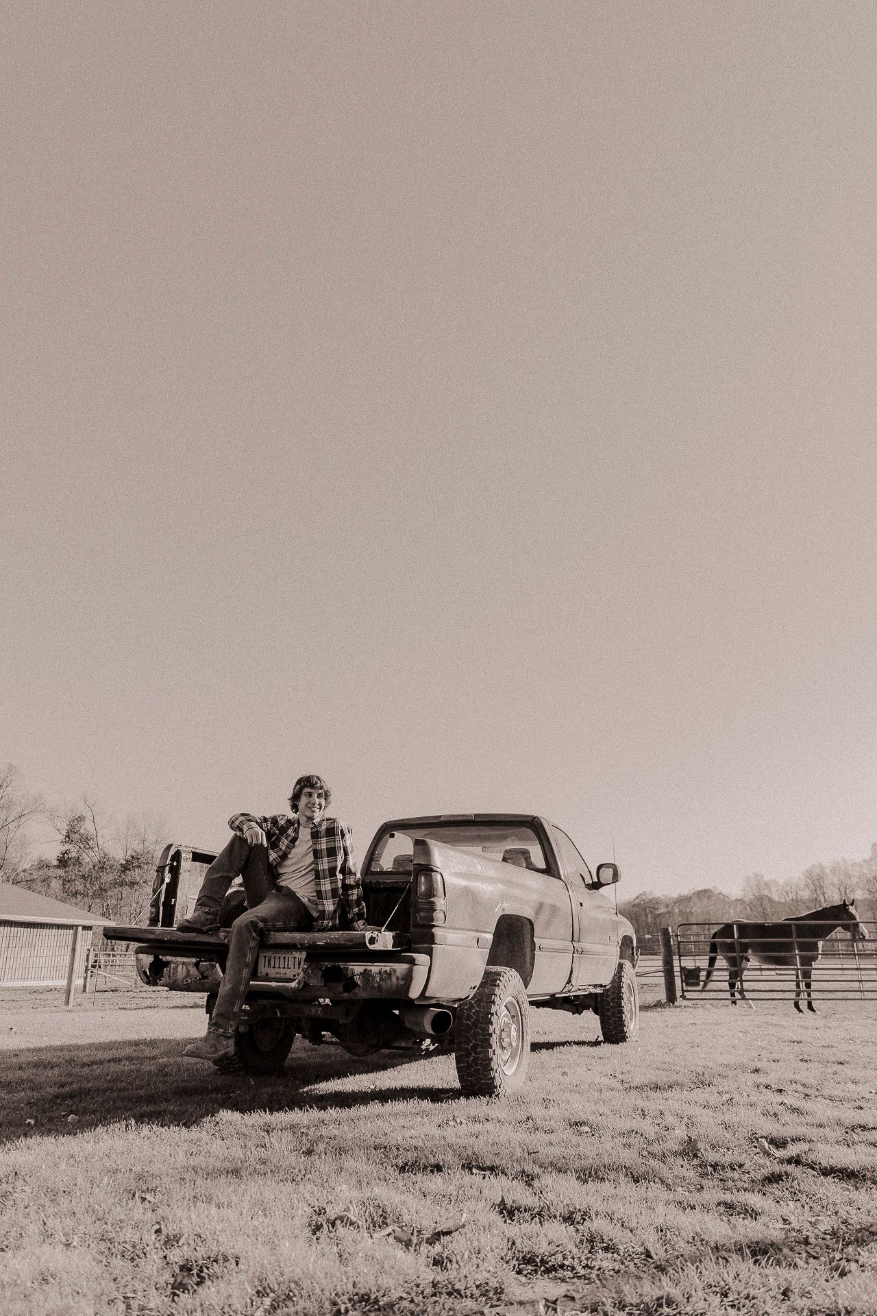 Person sitting on the tailgate of a pickup truck at a rural farm with a horse visible in the background.