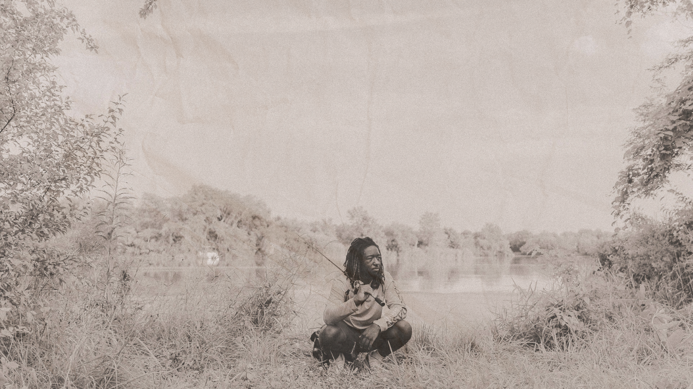 A sepia-toned vintage photograph shows a solitary figure sitting in a grassy meadow on a misty day.