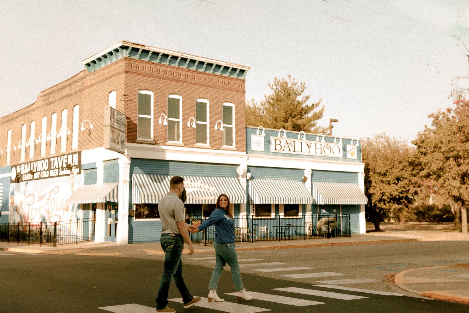 Couple holding hands crossing street in front of historic brick corner building with blue storefront in small town.